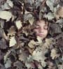 a young face partially covered with autumn leaves